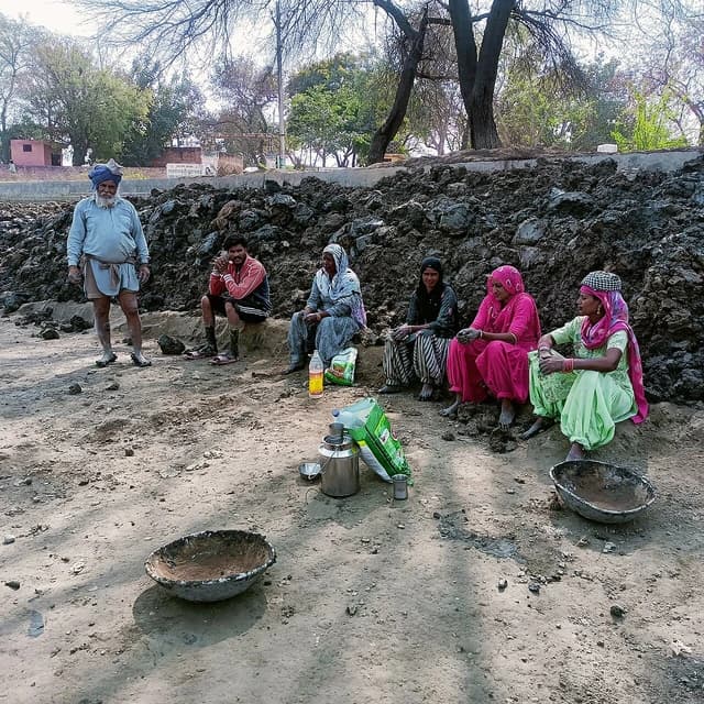 Group of laborers, two men and four women, resting on a dirt mound.