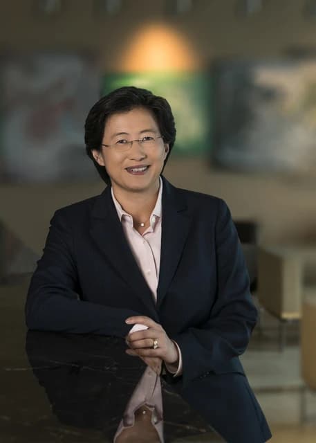 Lisa Su, CEO of AMD, stands and smiles while leaning on a dark surface.