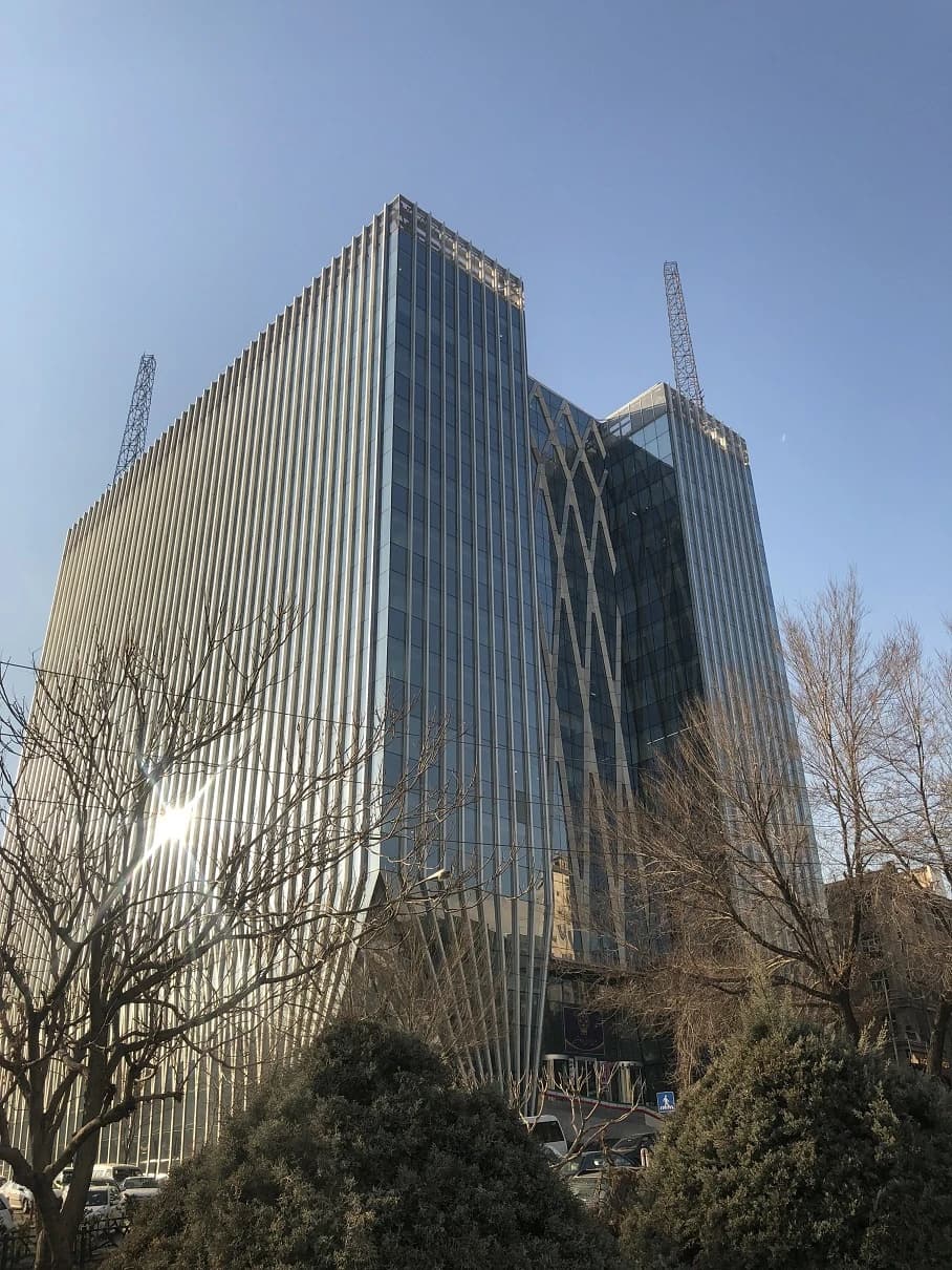 Modern glass and steel building of the Tehran Stock Exchange under a clear blue sky.