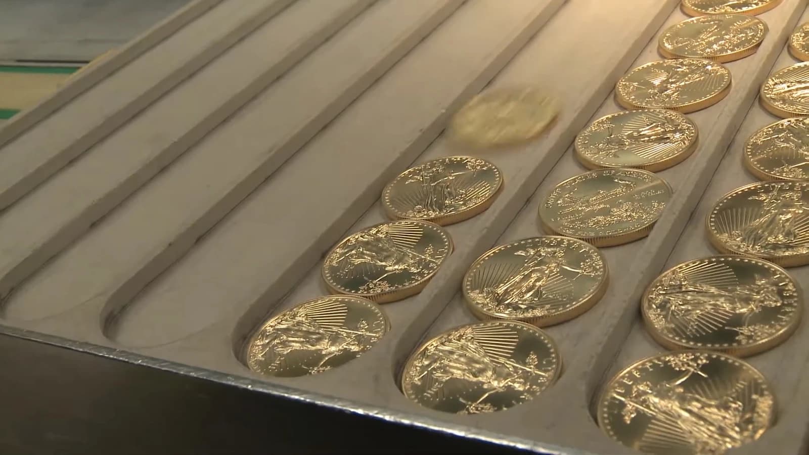 Several gold American Eagle coins, some arranged in rows, with one coin rolling.