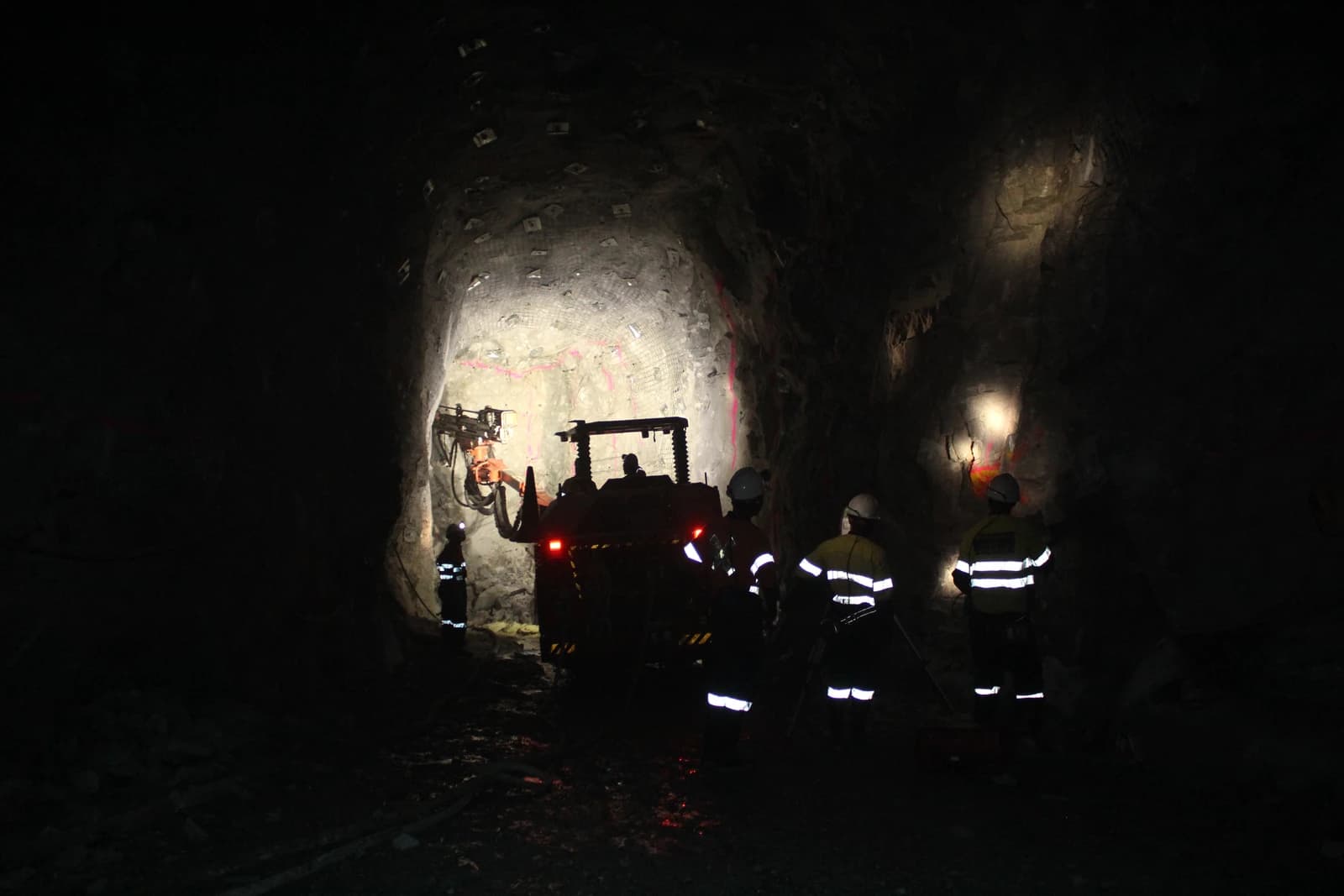 Miners operate machinery inside a dark underground mine tunnel.