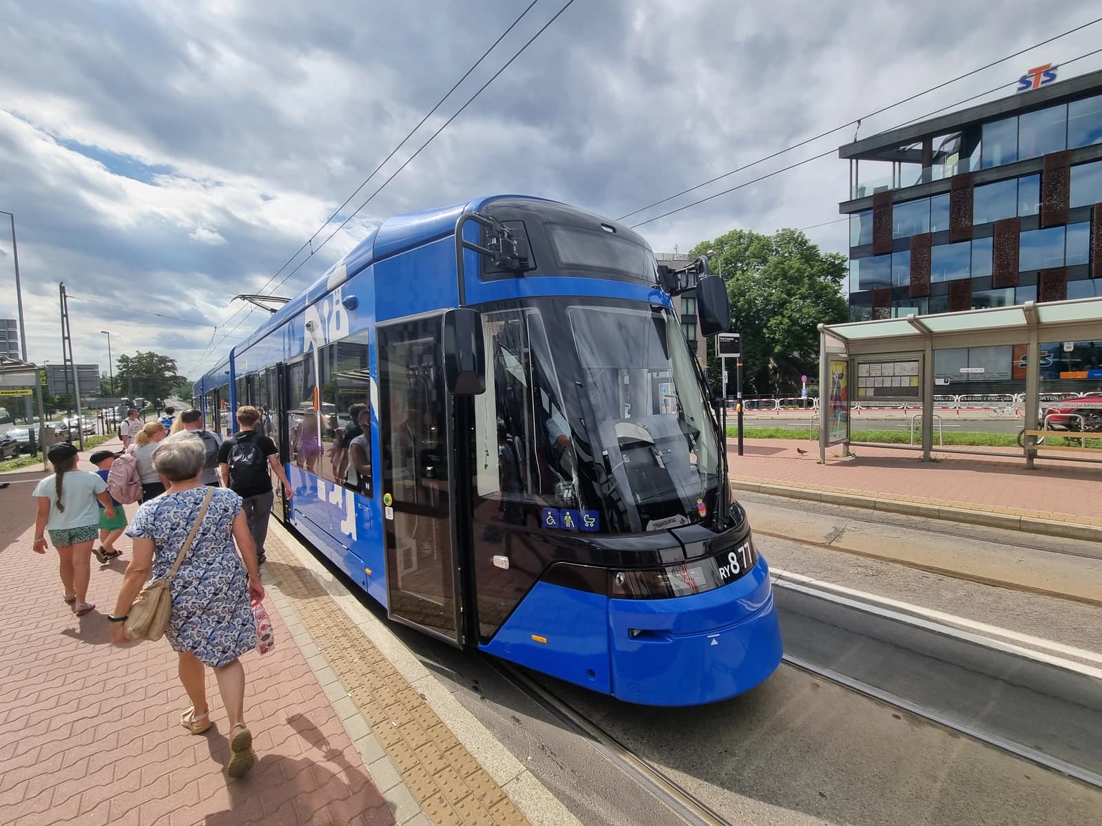 People boarding a modern blue tram at a tram stop in Krakow, Poland.
