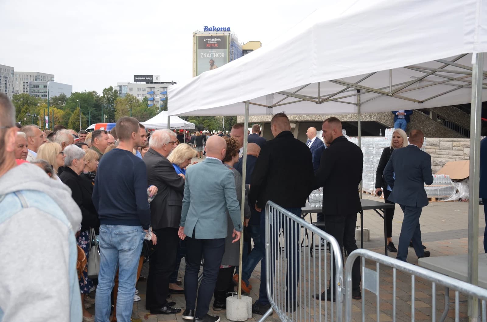 People attending a political rally or convention under tents in an urban setting.
