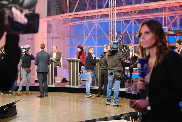 Journalists and politicians participating in a parliamentary debate, filmed by camera operators.
