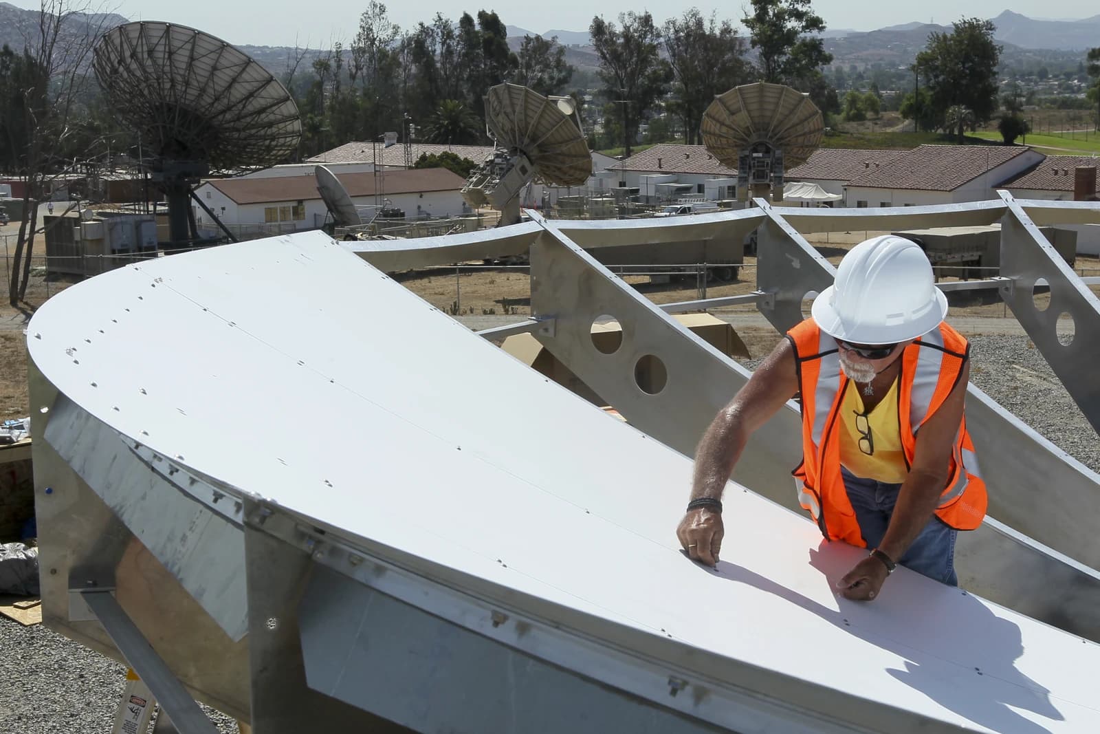 Worker in hard hat and safety vest assembling a satellite earth station antenna.