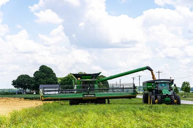 A combine harvester empties harvested wheat into a large grain cart on a sunny day.