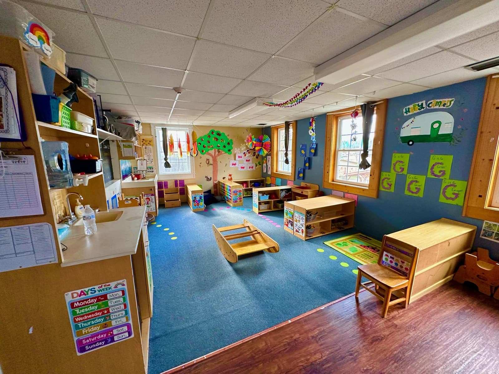An empty classroom in a child development center, with small tables, chairs, and play areas.