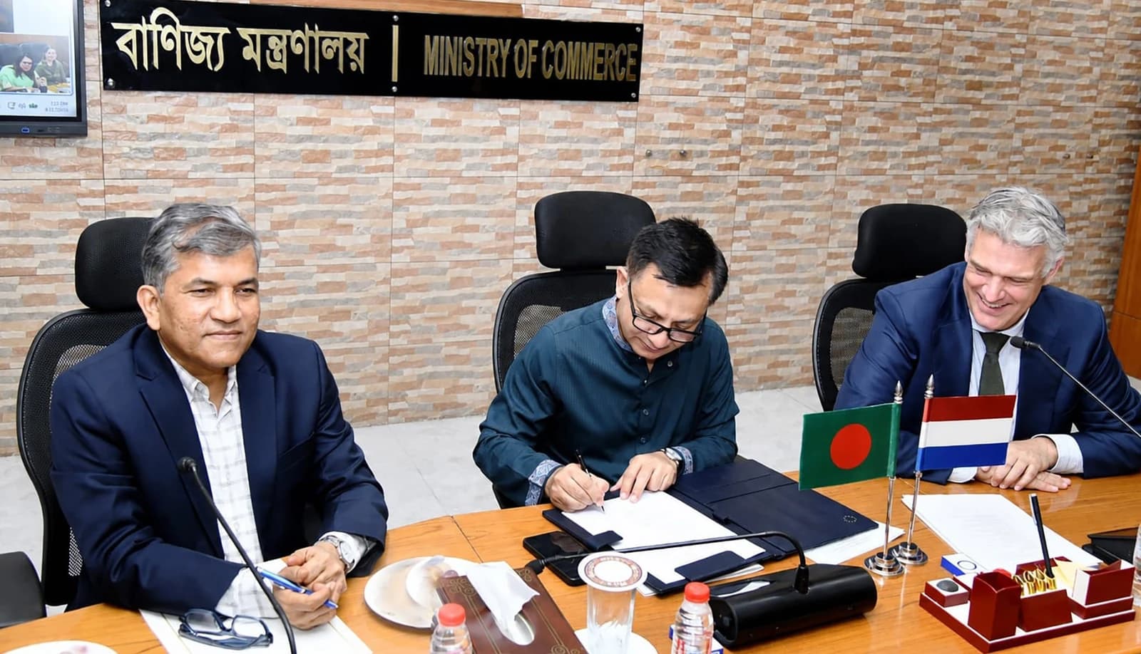Khandaker Abdul Muktadir signing a document at a meeting table with two other men.