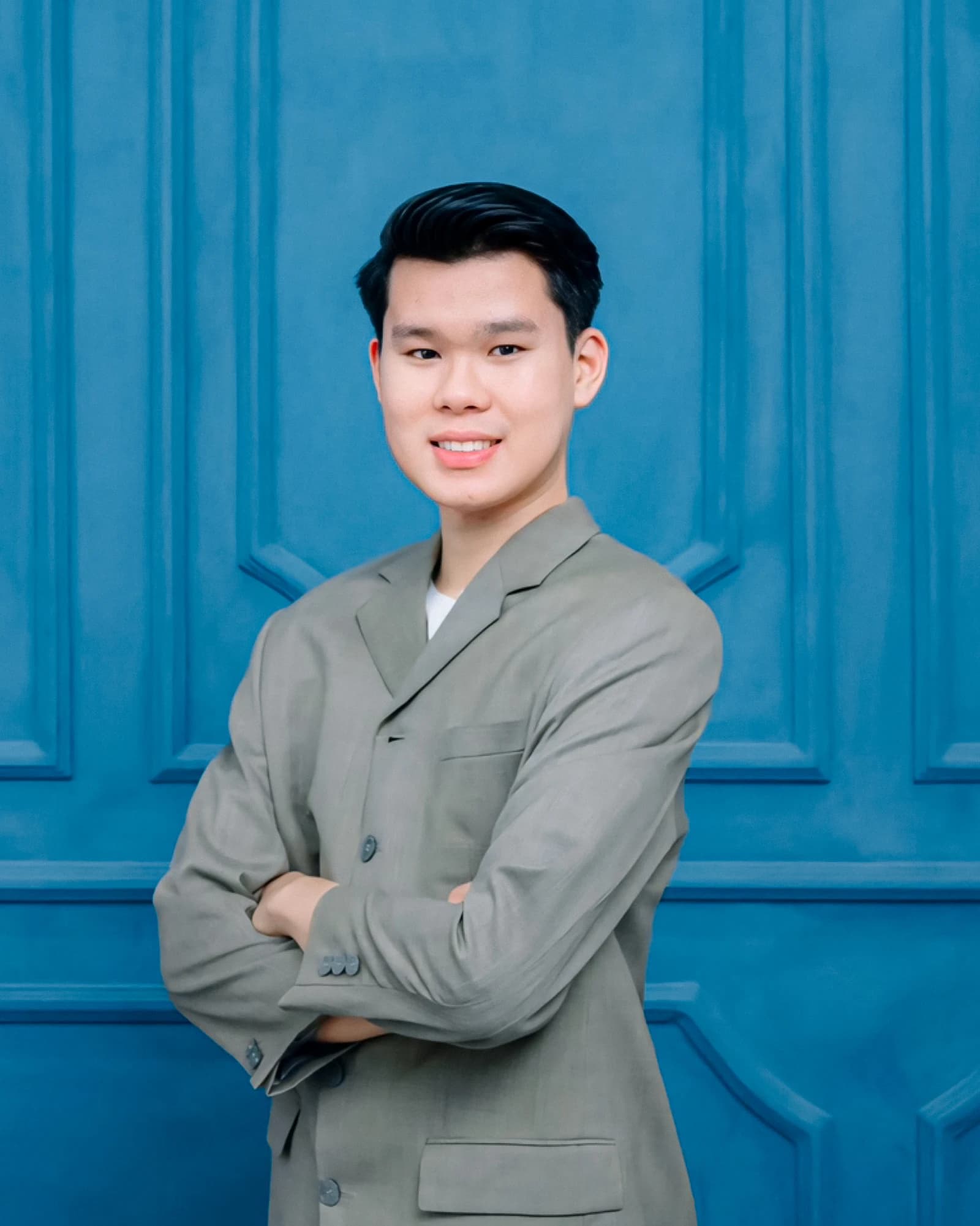 Deo Bernedy Putra, an individual, stands with arms crossed against a blue wall.