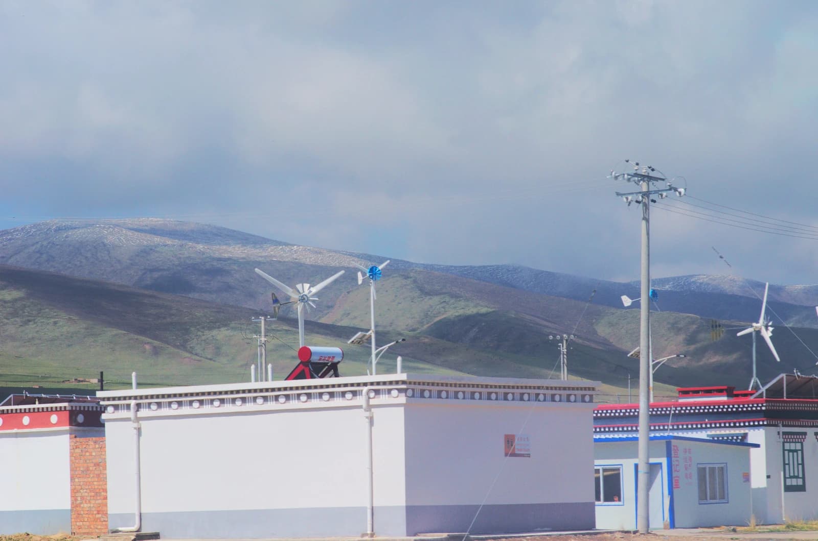 Buildings with small wind turbines and solar water heaters in front of hills.