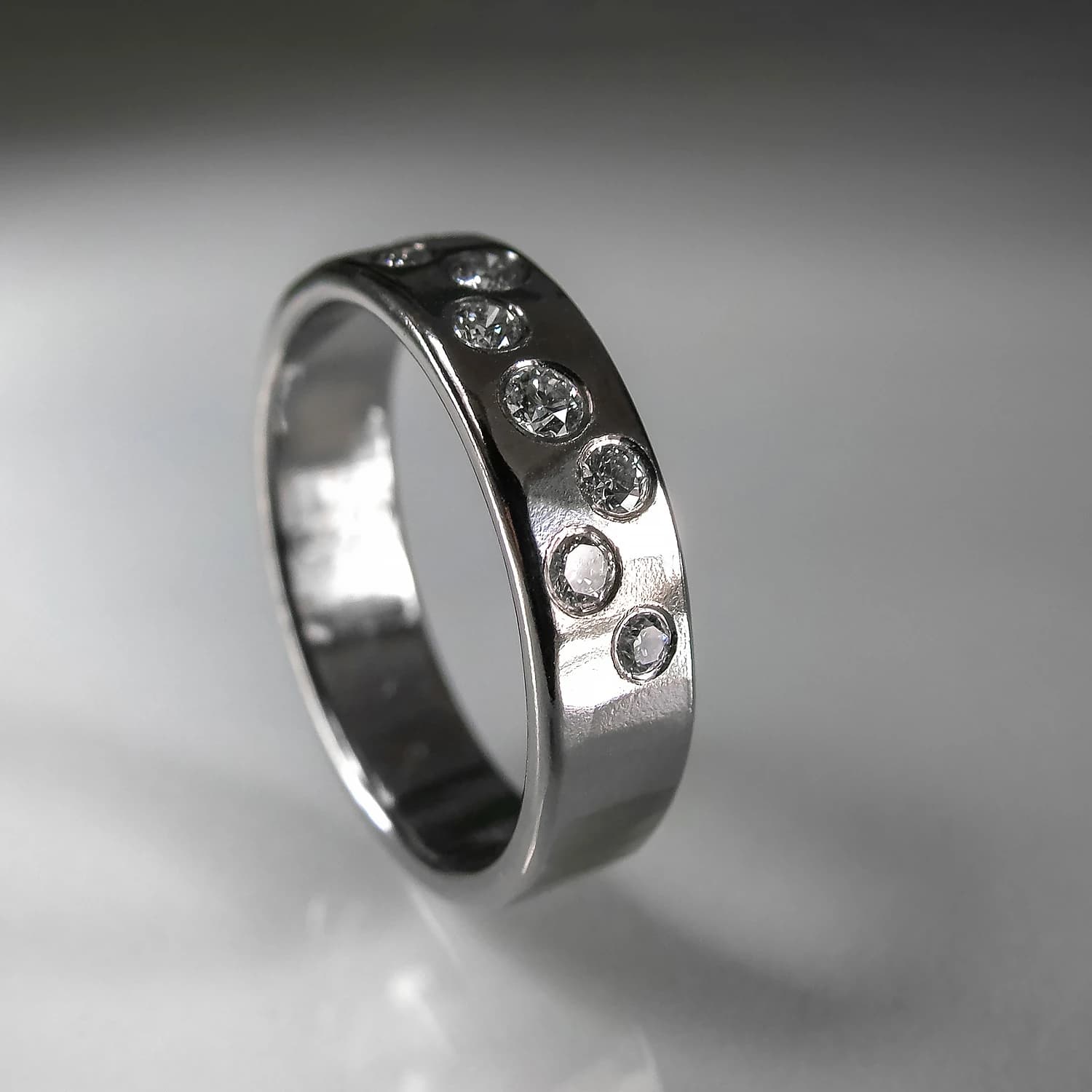 White gold ring with seven embedded diamonds rests on a reflective white surface.