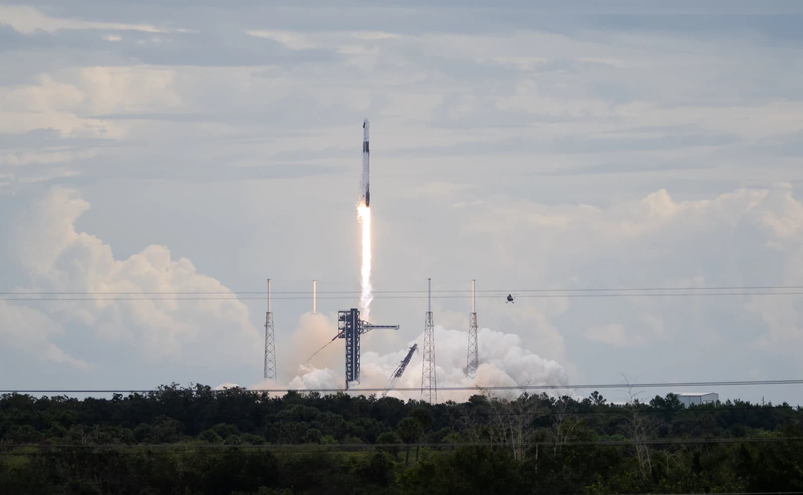 SpaceX rocket launching into a cloudy sky from a ground launchpad.