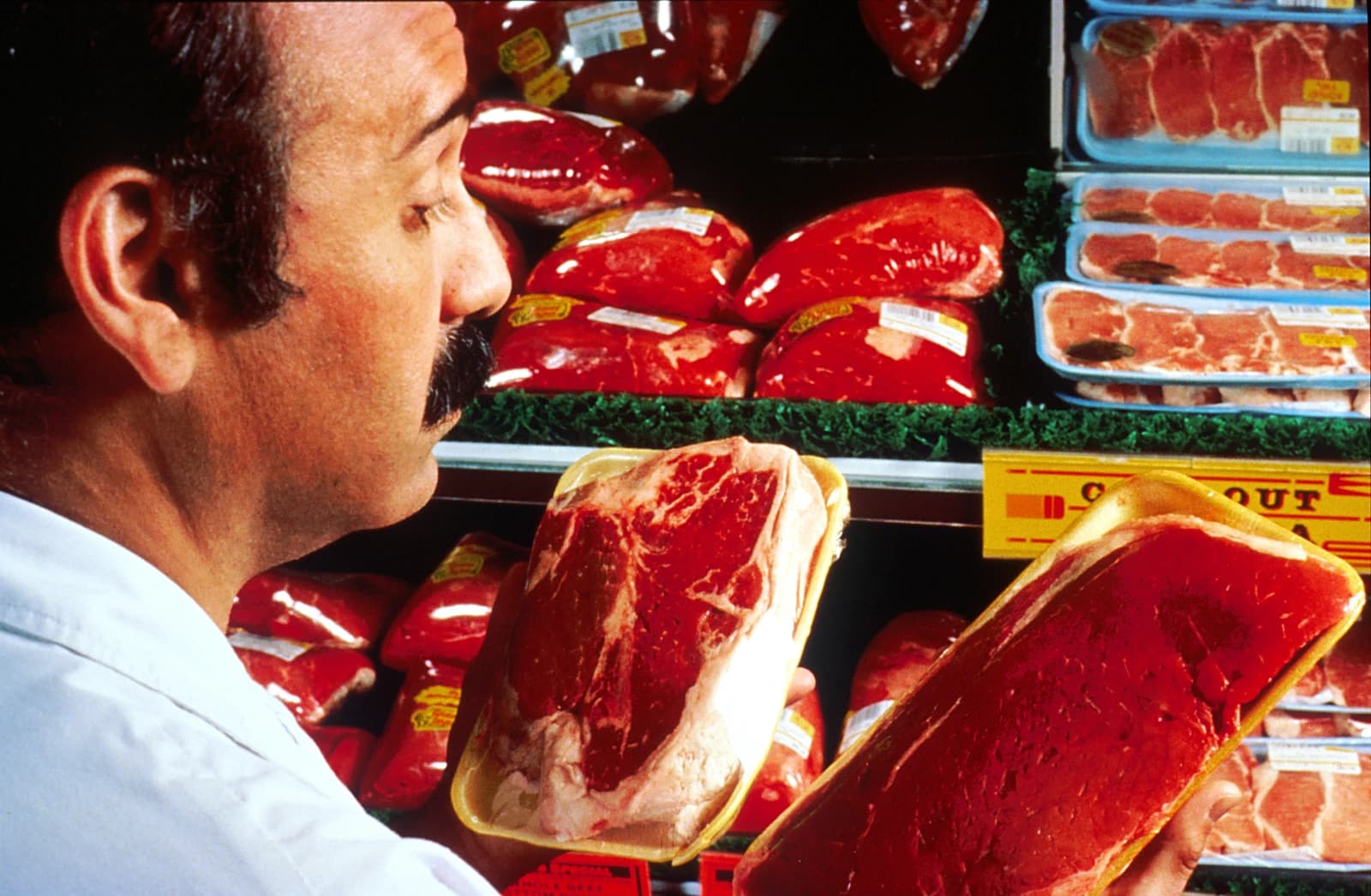 Man examines two packages of raw meat in a grocery store aisle.