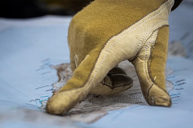 Military personnel wearing gloves points at a detailed map of a northern region.