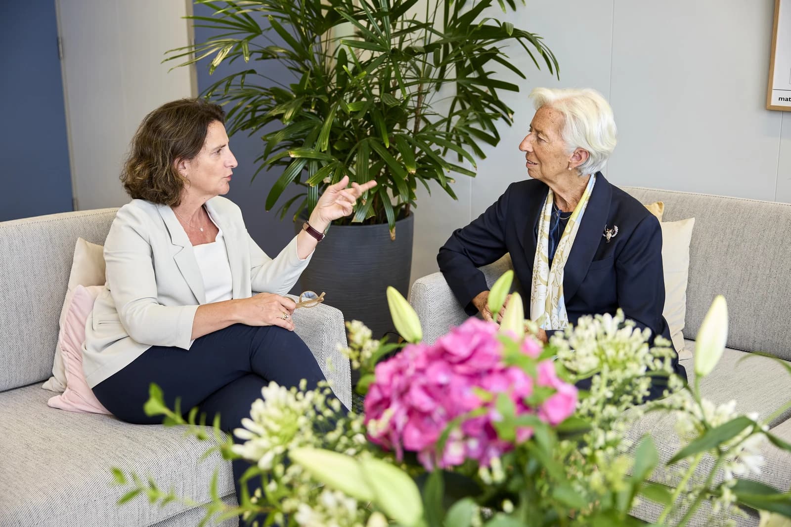Christine Lagarde, President of the European Central Bank, seated and listening to another woman.
