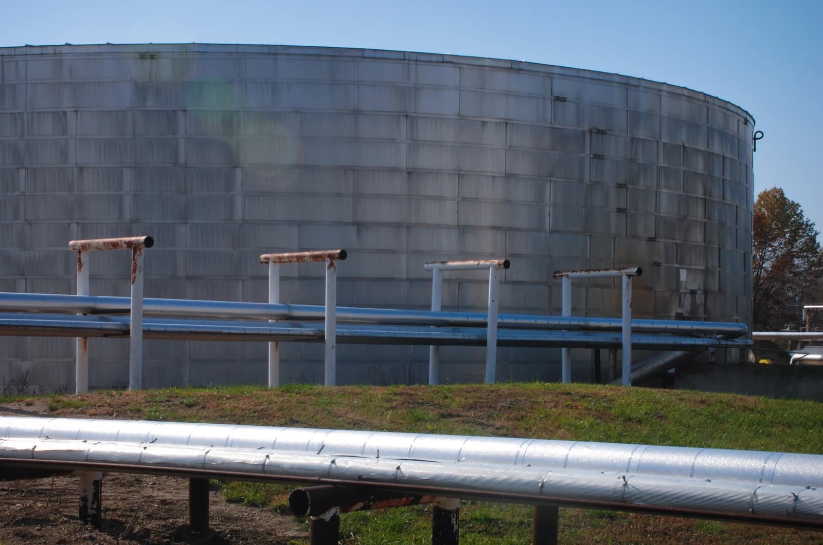Large cylindrical storage tank with corrugated metal exterior and multiple pipelines in the foreground.