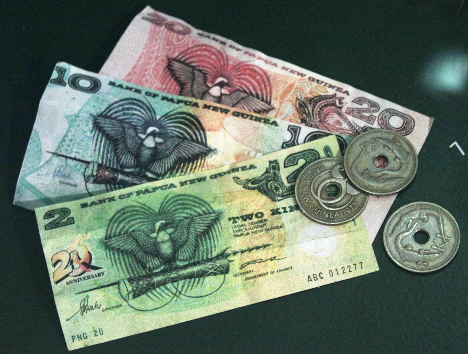 Papua New Guinean kina banknotes and coins displayed on a dark surface.