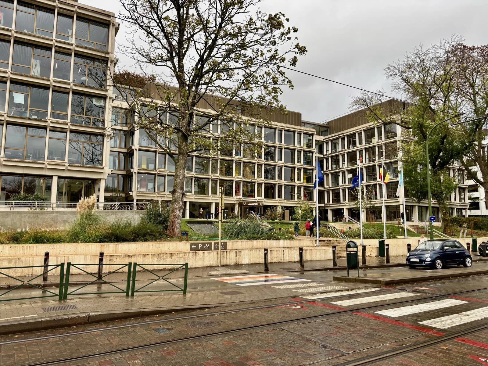 Uccle town hall building exterior with trees, street, and parked car on a cloudy day.