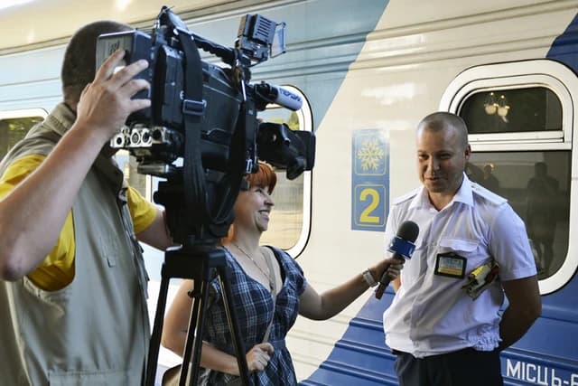 Man in white uniform being interviewed by a woman holding a microphone, with a cameraman filming.