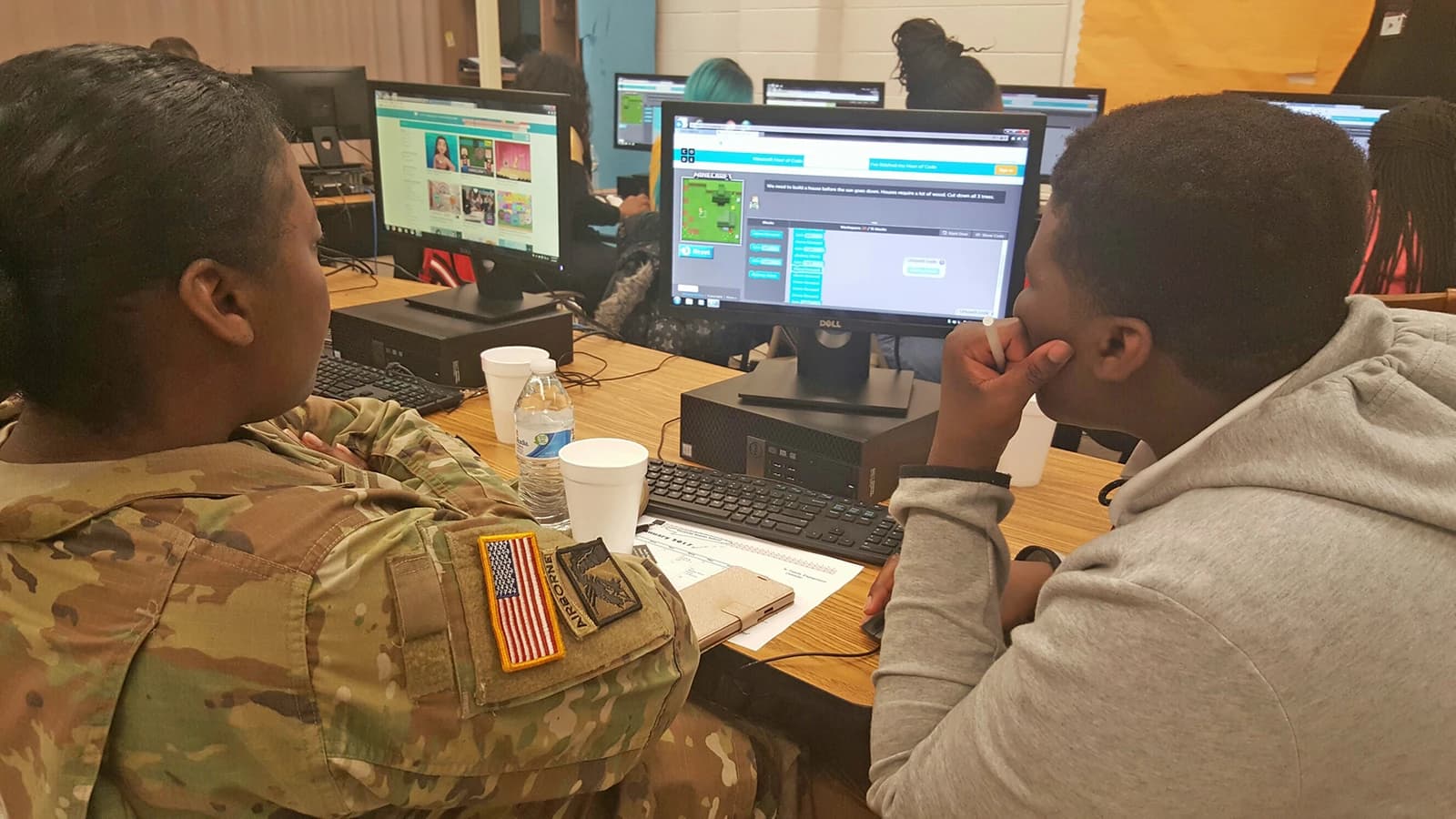An adult in military uniform and a student sit at computers, looking at screens.