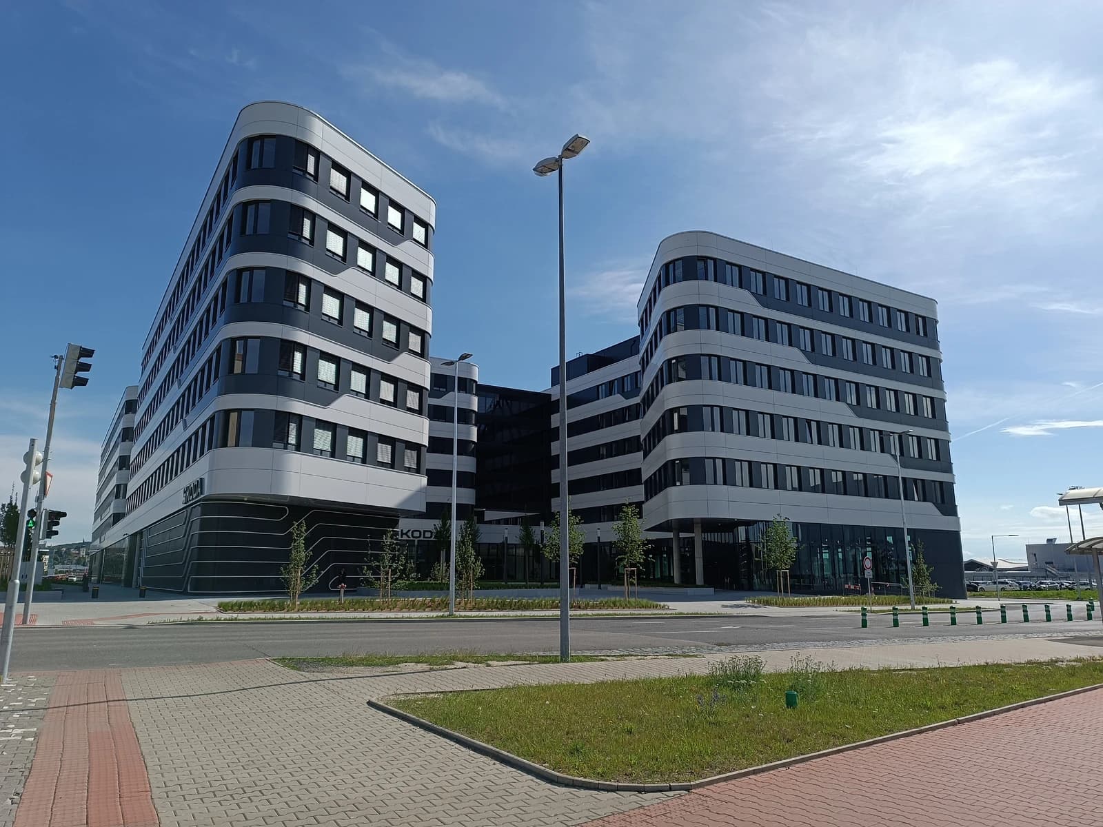 Modern multi-story corporate building with dark windows and a curved facade, labeled 'ŠKODA'.