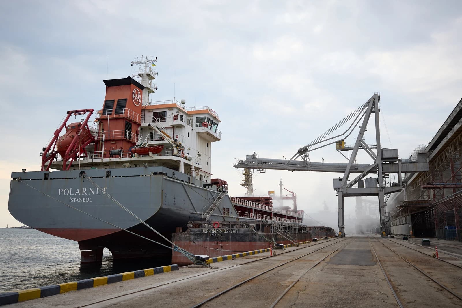 Cargo ship Polarnet docked at a port with loading cranes overhead.
