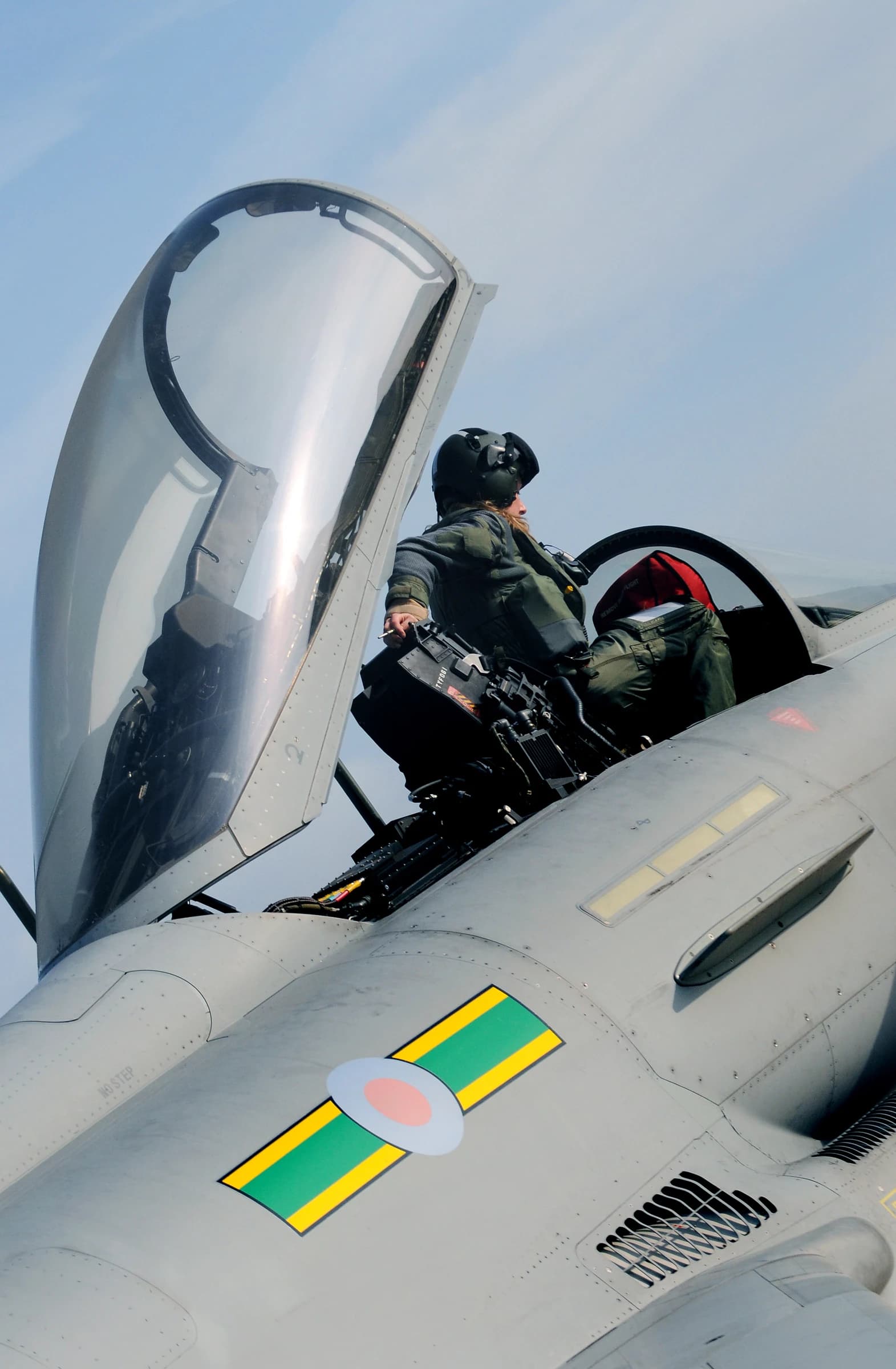 RAF Typhoon pilot wearing a helmet and flight suit climbs into the cockpit of a fighter jet.