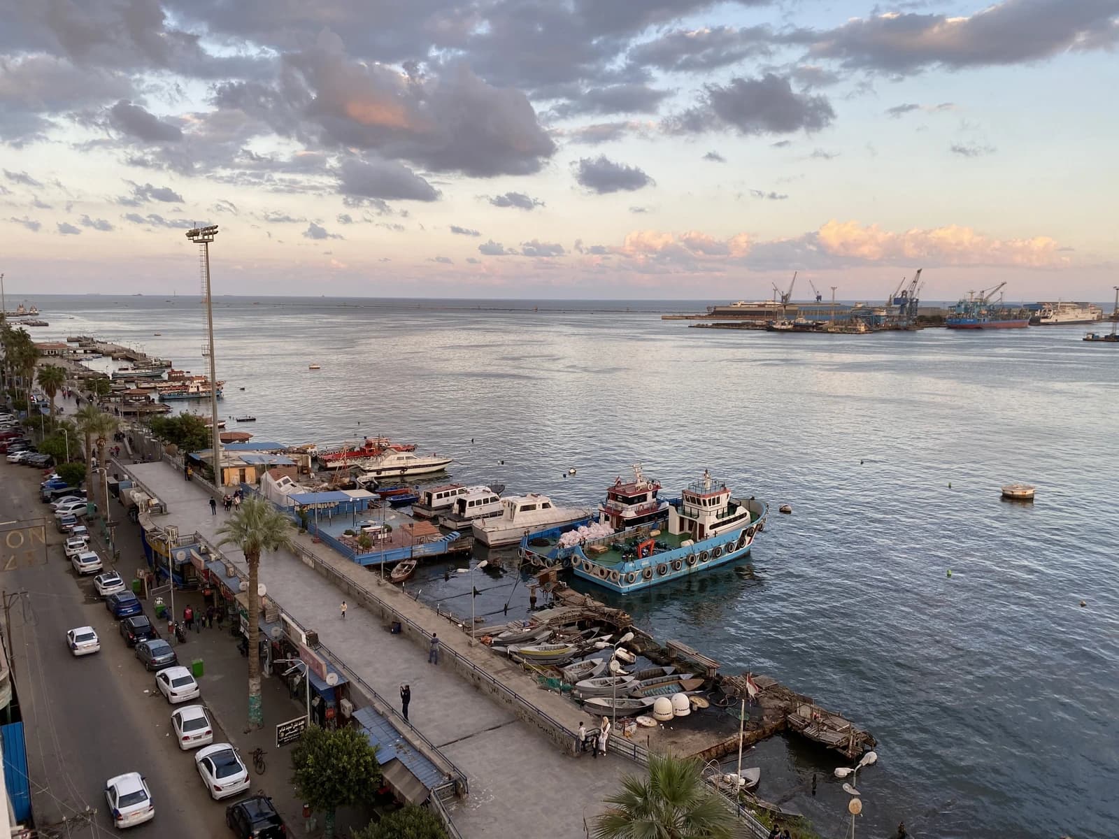 Suez Canal entrance at dusk, with boats docked and port cranes in the background.
