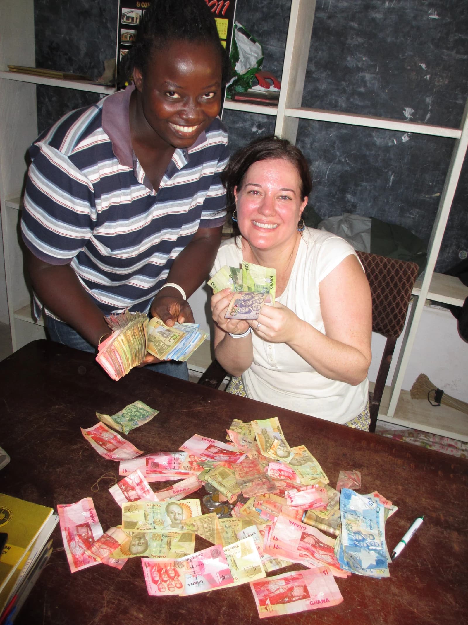 Two people holding and sorting through Ghanaian Cedi banknotes on a wooden table.