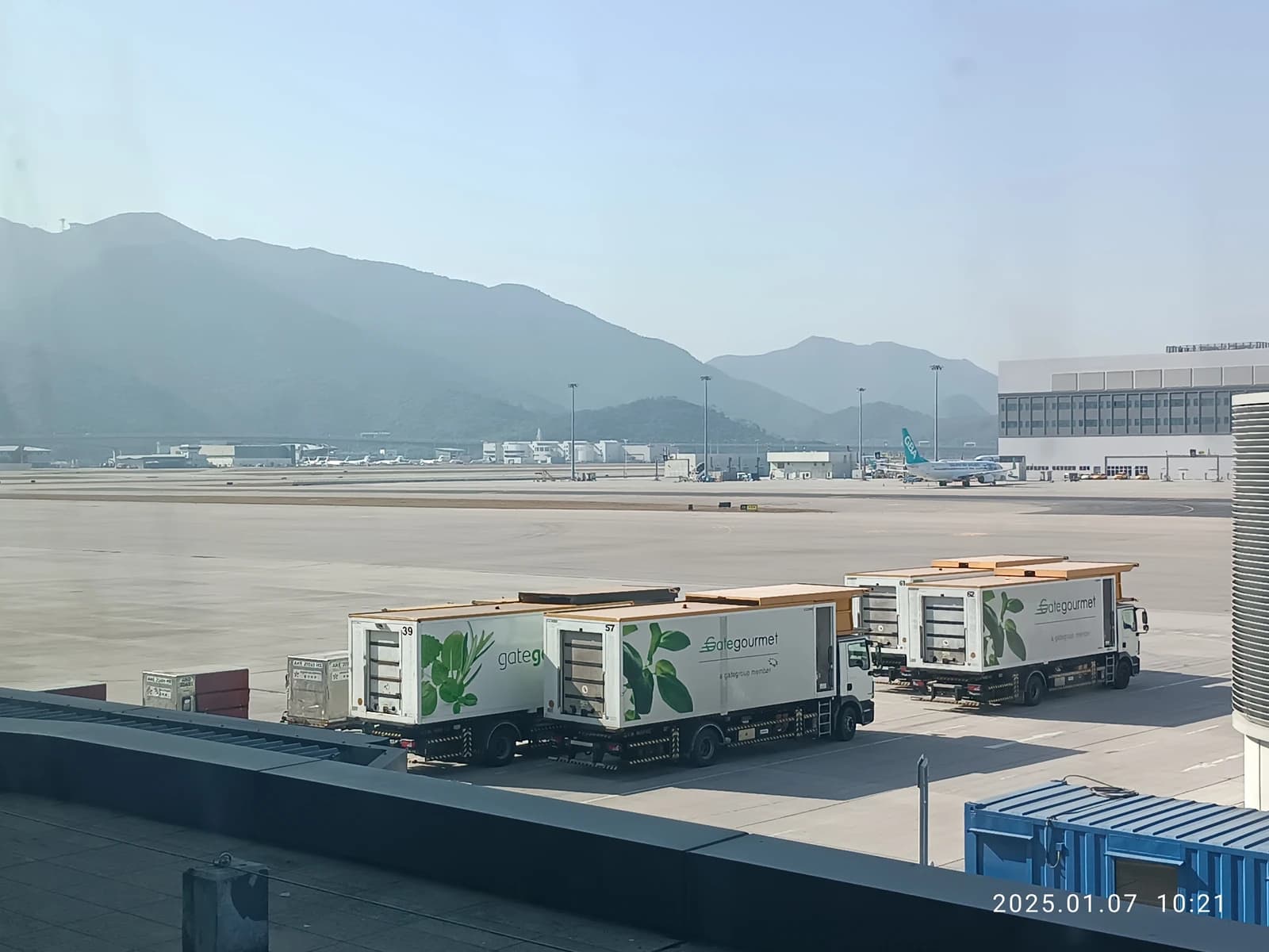 Ground support vehicles and distant aircraft on the tarmac at Hong Kong International Airport.