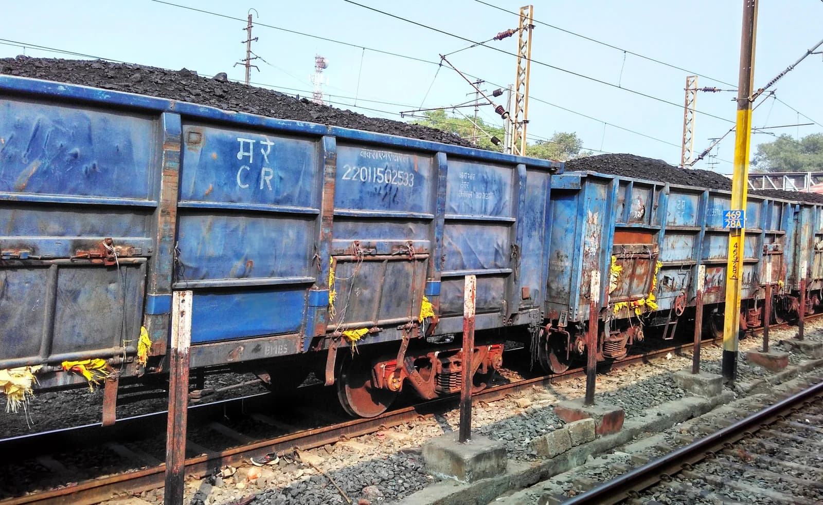 Open-top freight wagons filled with coal on railway tracks under electrical lines.