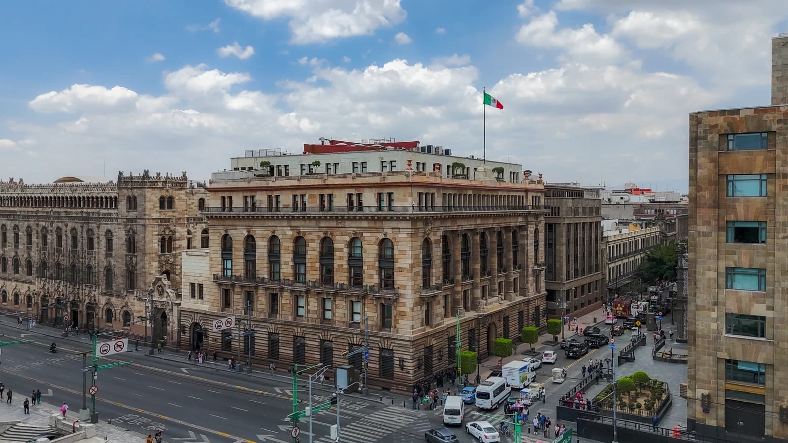Aerial view of the Banco de México building, a large stone structure with a Mexican flag on its roof.