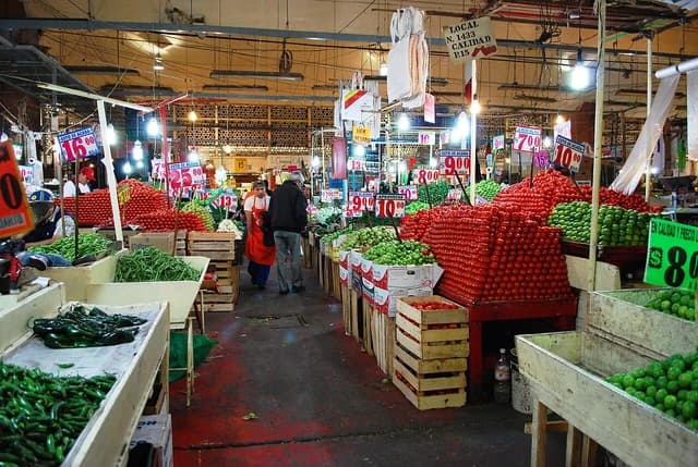 Produce vendor arranging green and red tomatoes at an indoor market.