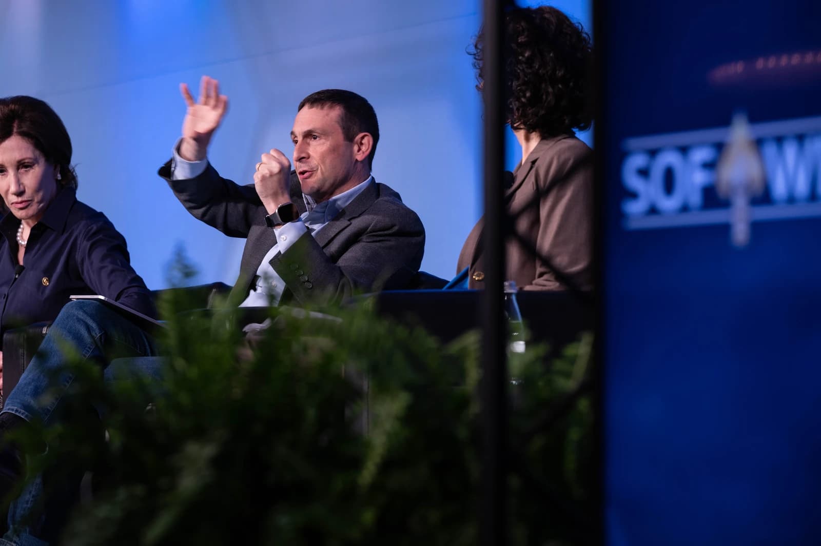 Doug Beck speaking into a microphone, gesturing with his hand at a conference.