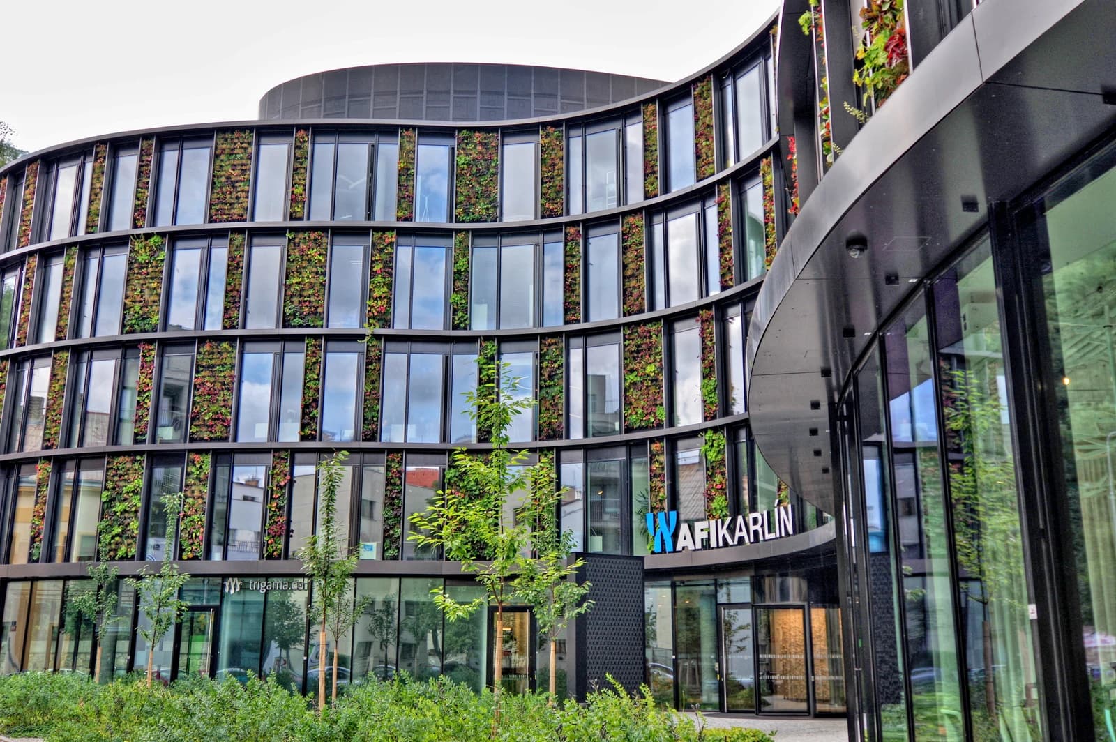 Modern office building named AFI Karlín with a facade featuring numerous green plants.