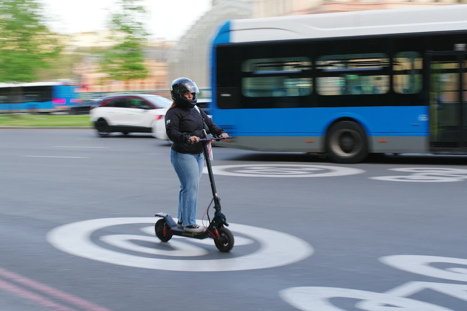 Woman in a helmet riding an electric scooter on a city street.