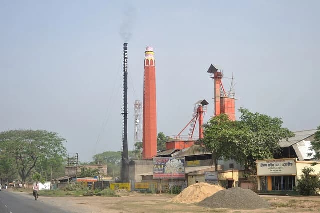 An industrial rice mill facility with smokestacks and processing machinery in rural India.