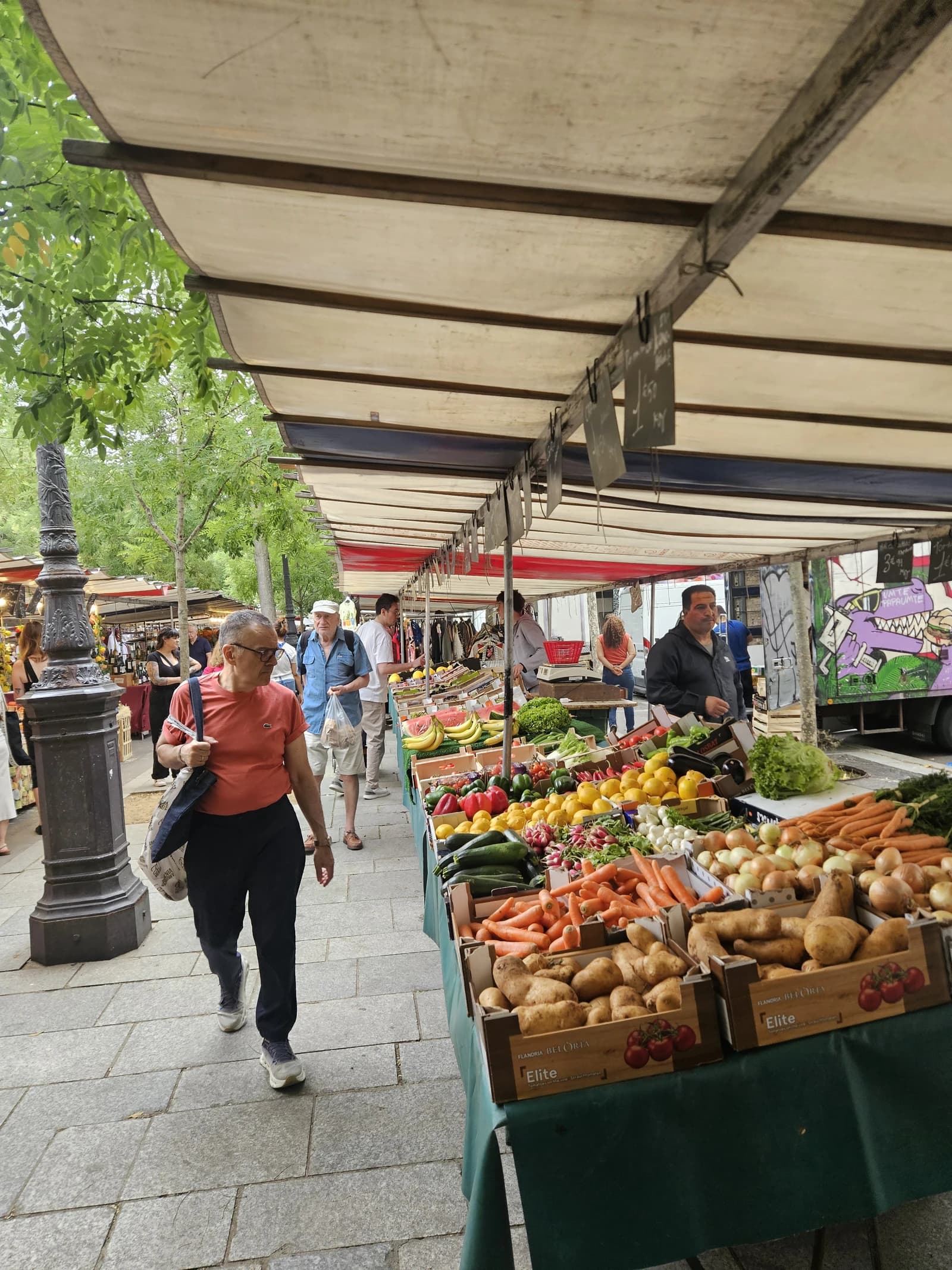People browse colorful displays of fresh fruits and vegetables at an outdoor market stall.