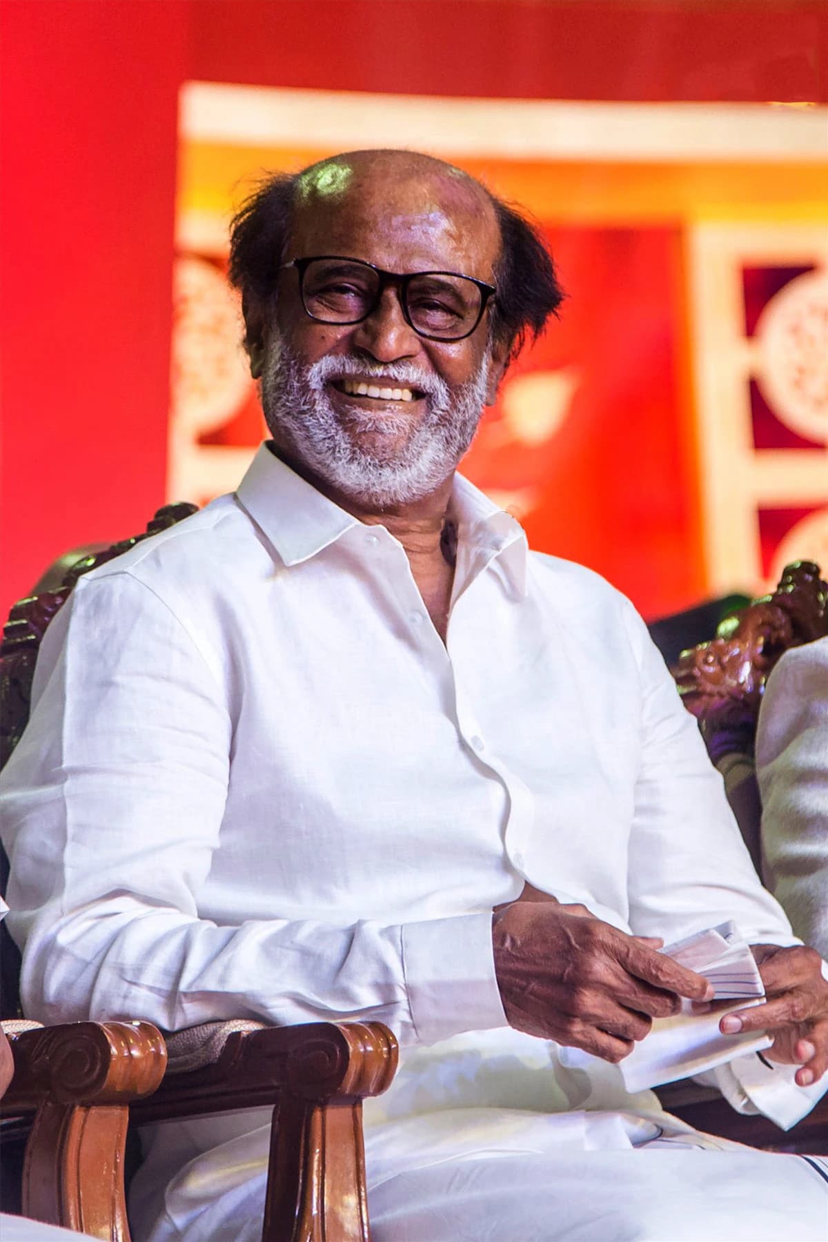 Rajinikanth, Indian actor, smiling while seated at an event.