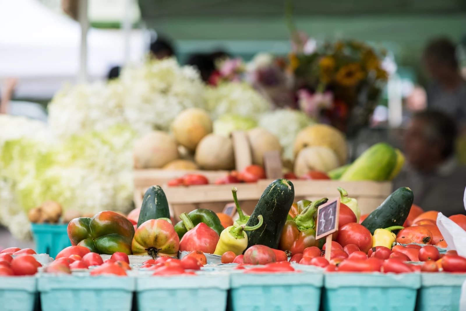 Colorful vegetables, including peppers, tomatoes, and gourds, displayed at a market stall.