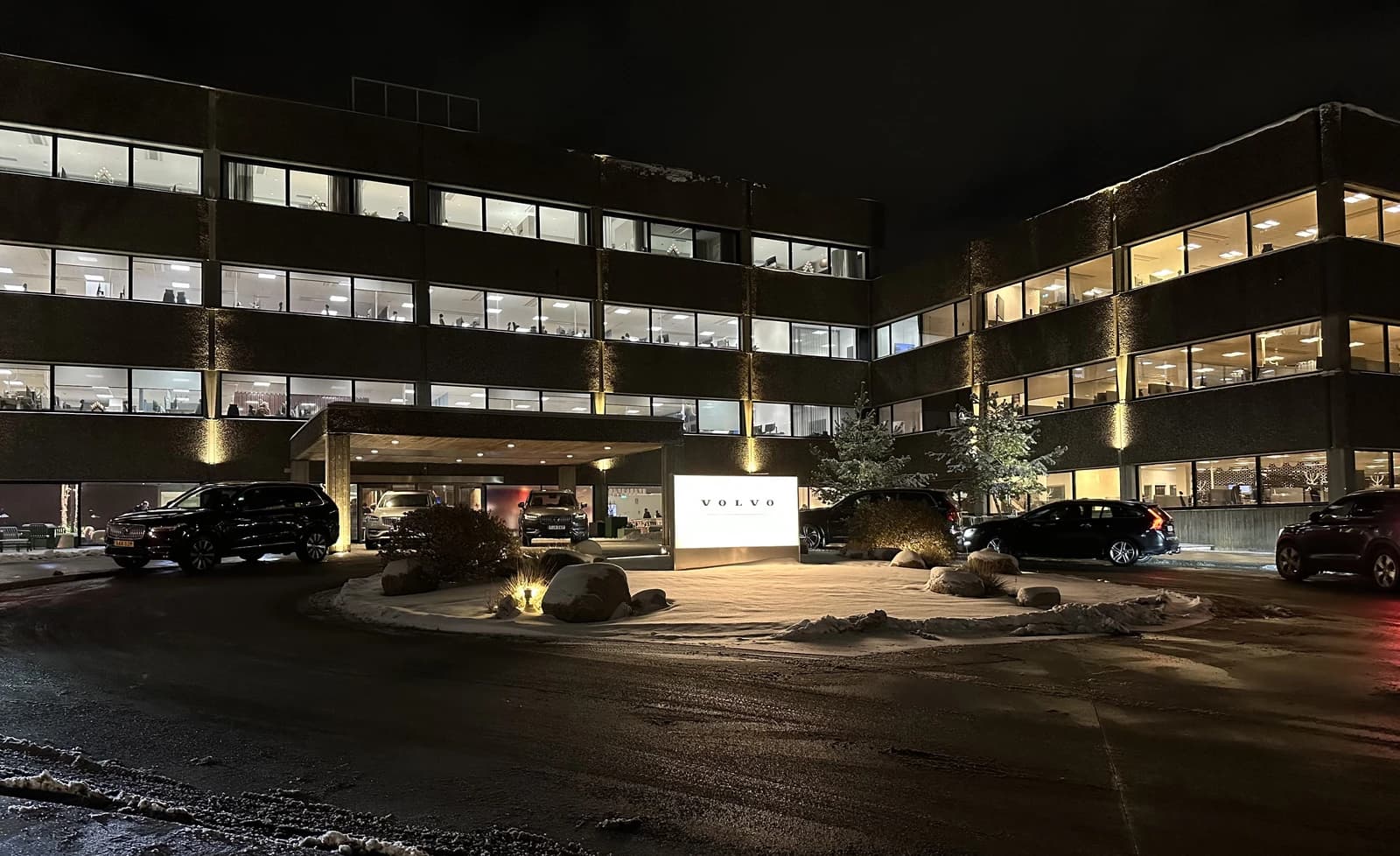 Exterior of the Volvo Cars headquarters building at night, with illuminated windows and a 'VOLVO' sign.
