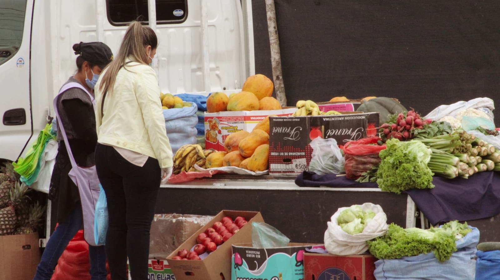 Customers at a mobile market stall displaying fresh fruits and vegetables.