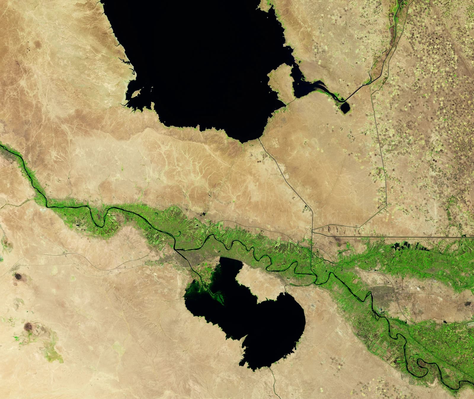 Aerial view shows dark water bodies and green river winding through arid landscape.