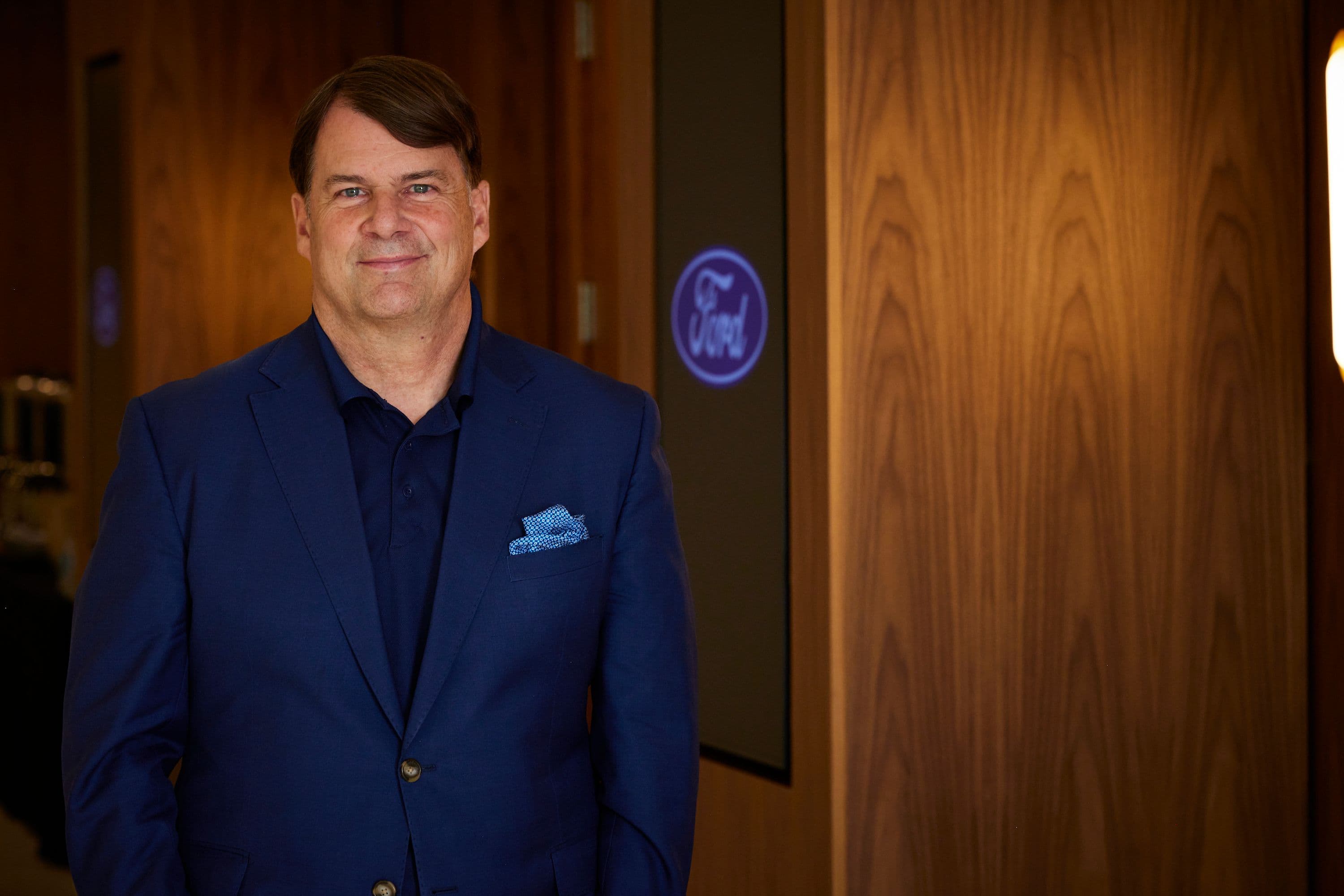Jim Farley, CEO of Ford, standing in front of a wood-paneled wall.
