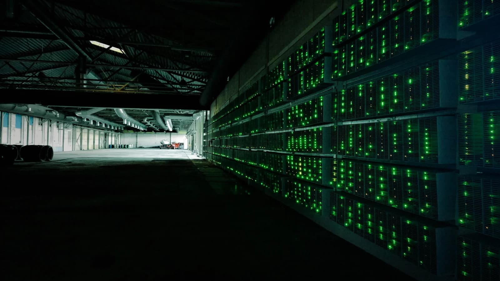 Cryptocurrency mining machines with green lights operating in a large dark facility.