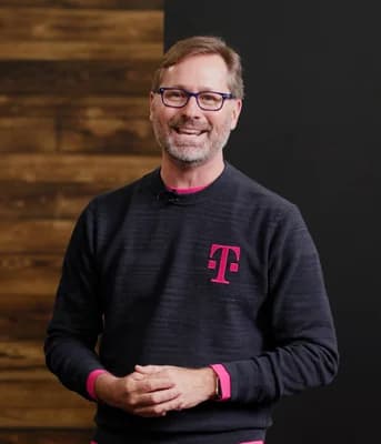 Mike Sievert, CEO of T-Mobile, standing and smiling in an indoor setting.