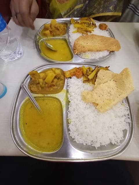 Vegetarian Indian thali with white rice, yellow dal, and potato curry served on a metal plate.