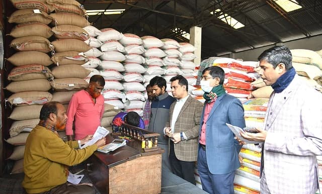 Ministry of Food officials and market workers in a warehouse filled with sacks of grain.