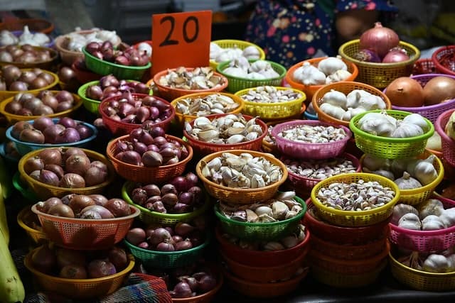 Baskets filled with red onions, white onions, and garlic cloves at a market stall.