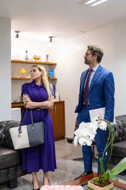 Tereza Cristina stands with a governor in an office setting, both looking away.